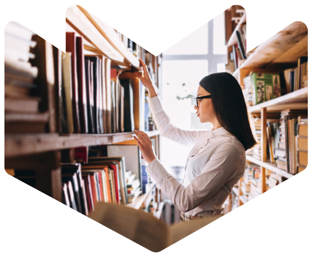 A women standing in front of a bookshelf reaching out to take a book from the shelf.